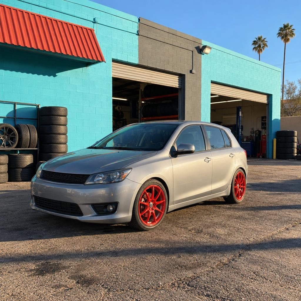 Silver hatchback with red wheels in front of the shop